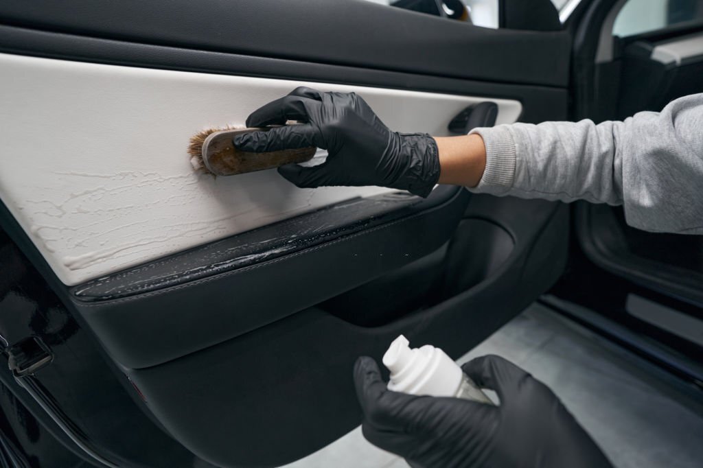 Cropped photo of worker cleaning car door panel coated with automotive soap