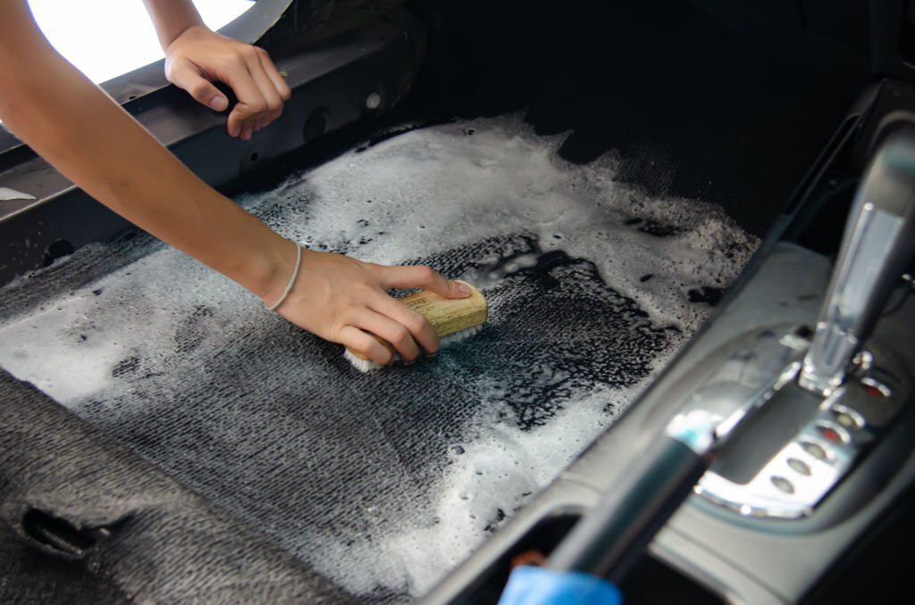 Wash the car carpet.Detailing on interior of modern car.Clean by using a brush and cleaning solution on the car carpet.