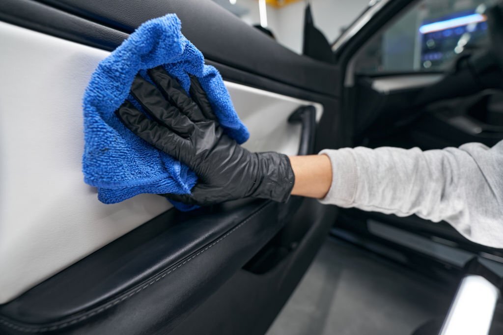 Cropped photo of detailer wiping down inner surface of auto door panel