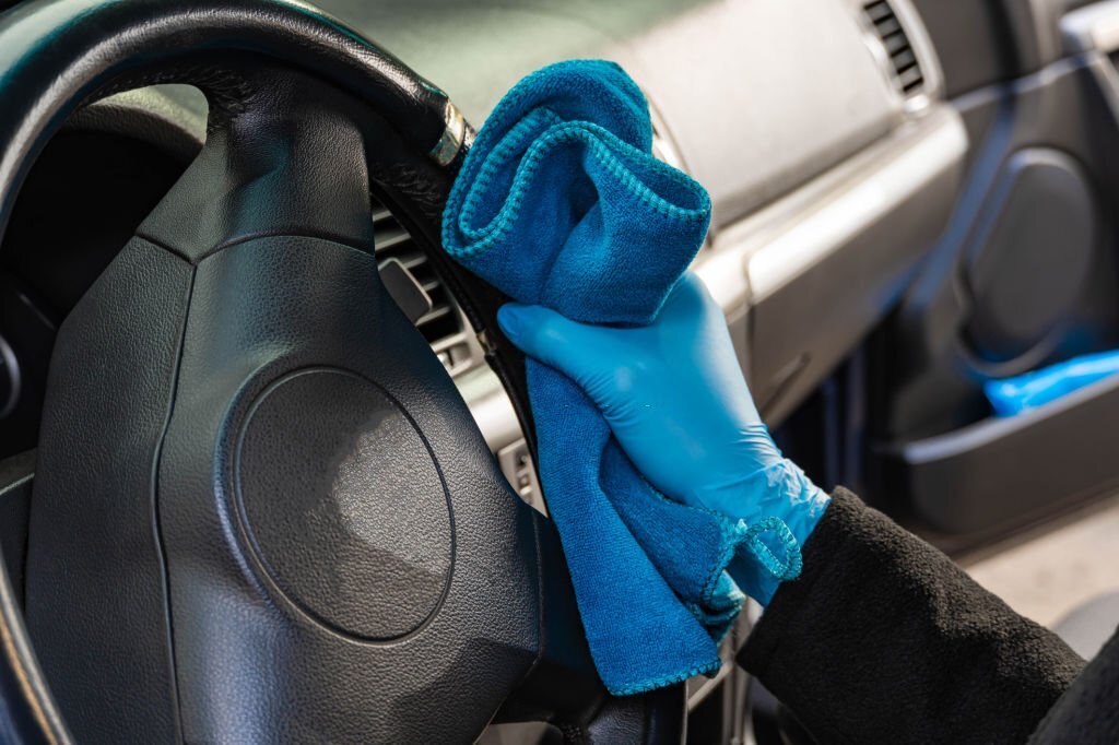 Hands in blue rubber gloves rub the steering wheel of a car. Car interior cleaning. Close-up