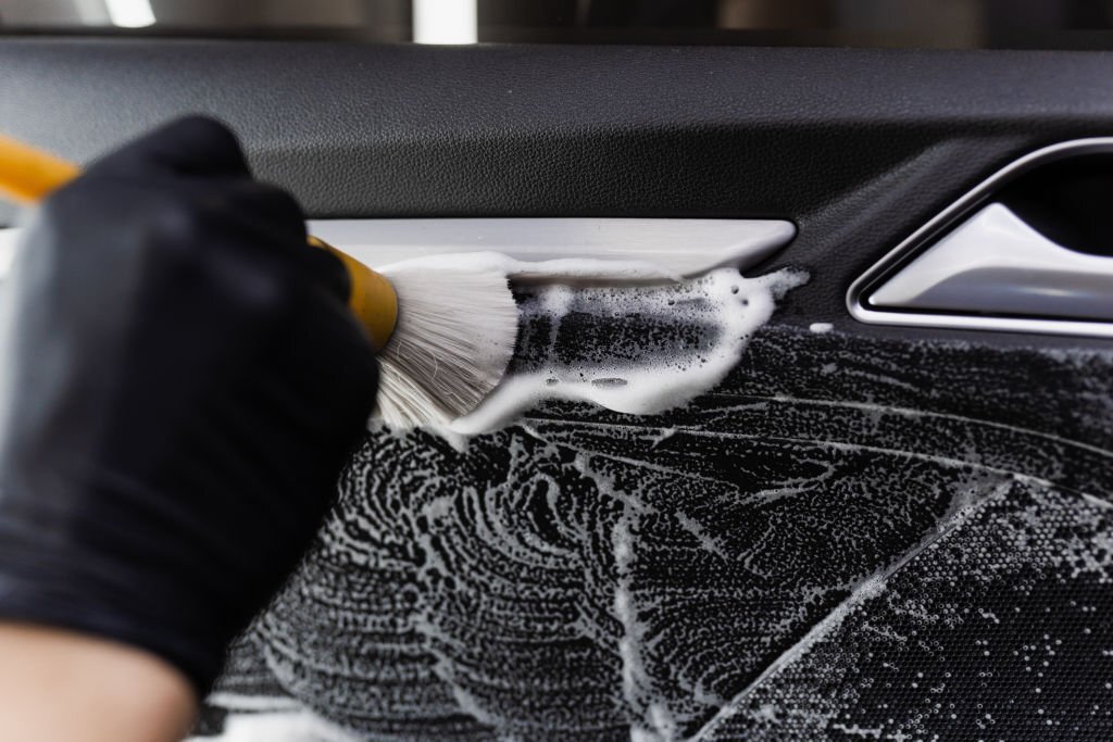 Foam and detergent washing using brush inside handle of car door. Car detailing service. Worker in cleaning service wash leather interior of clients auto