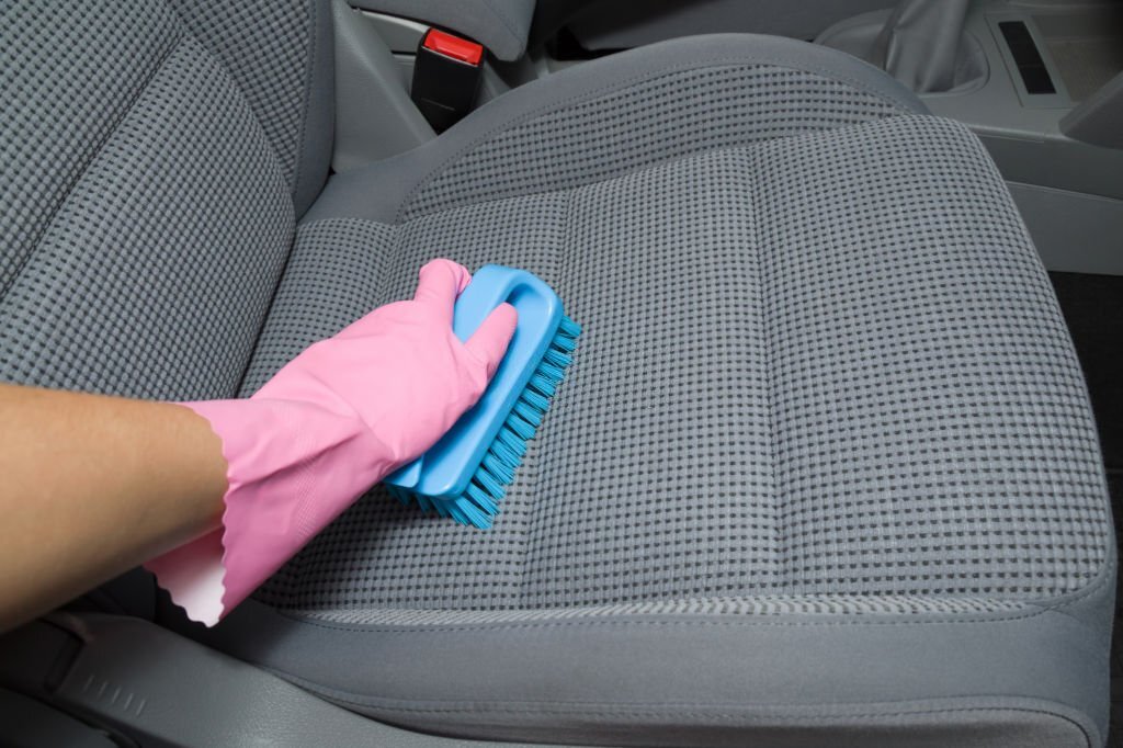 Employee hand in rubber protective glove cleaning textile seat with professionally brush. Regular cleanup. Care about auto interior. Commercial cleaning company concept. Point of view shot.