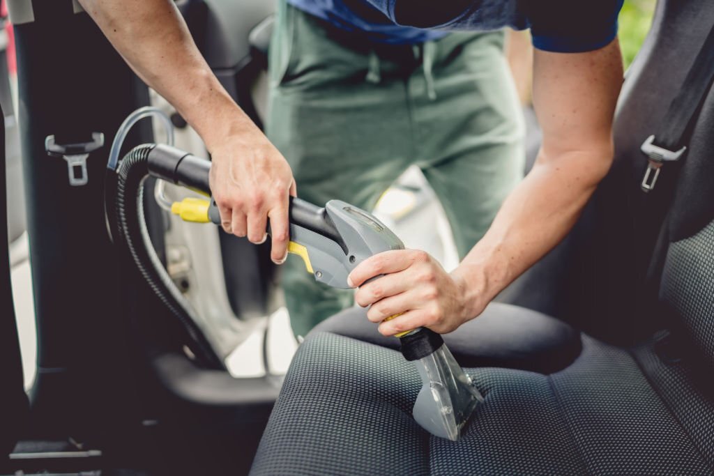 Details of car cleaning - male using professional steam vacuum for dirty car interior