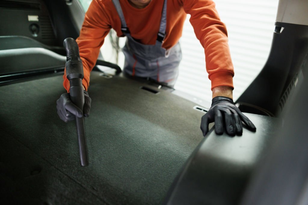 Close up shot of young unrecognizable car detailer vacuuming car trunk and seat