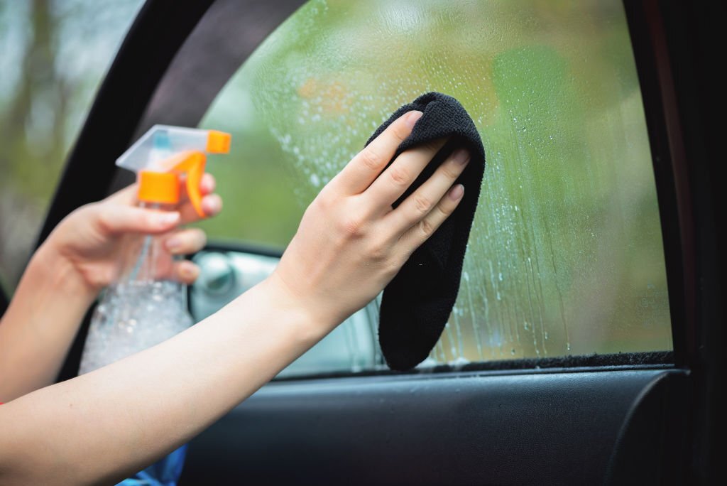 Cleaner is cleaning a car window glass with a rag and detergent close up.