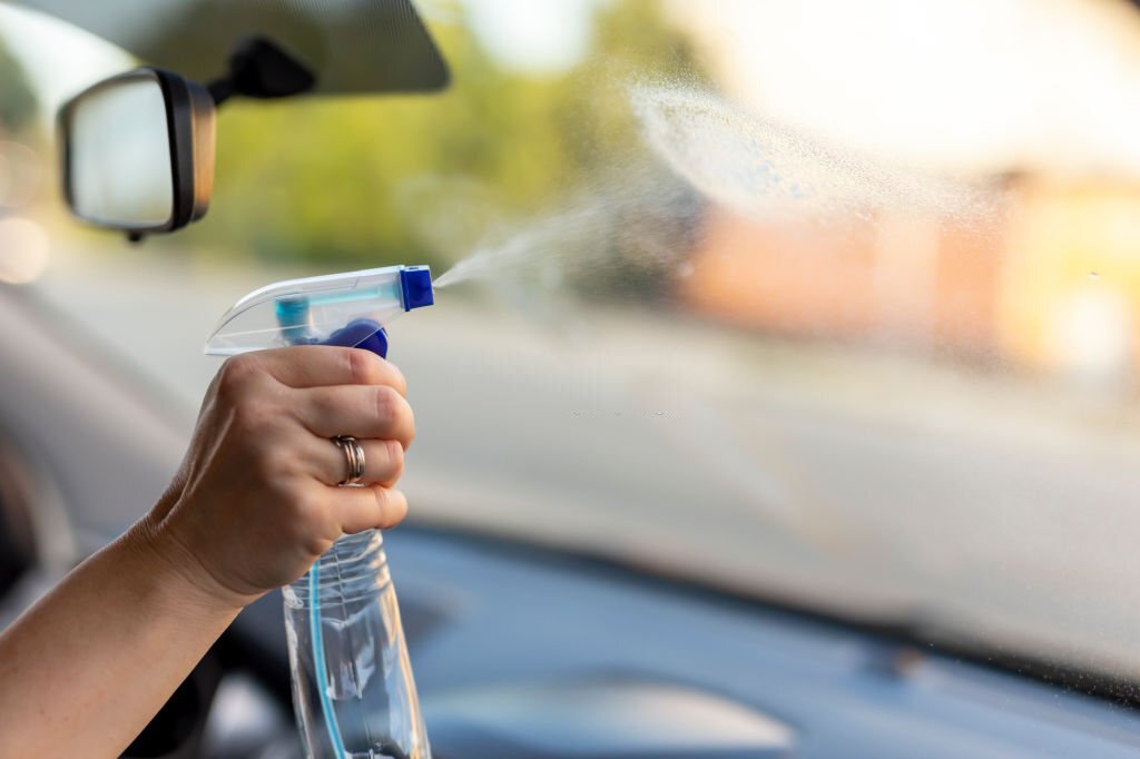 Detail of female hand cleaning a car windshield while washing car with cleanser spray