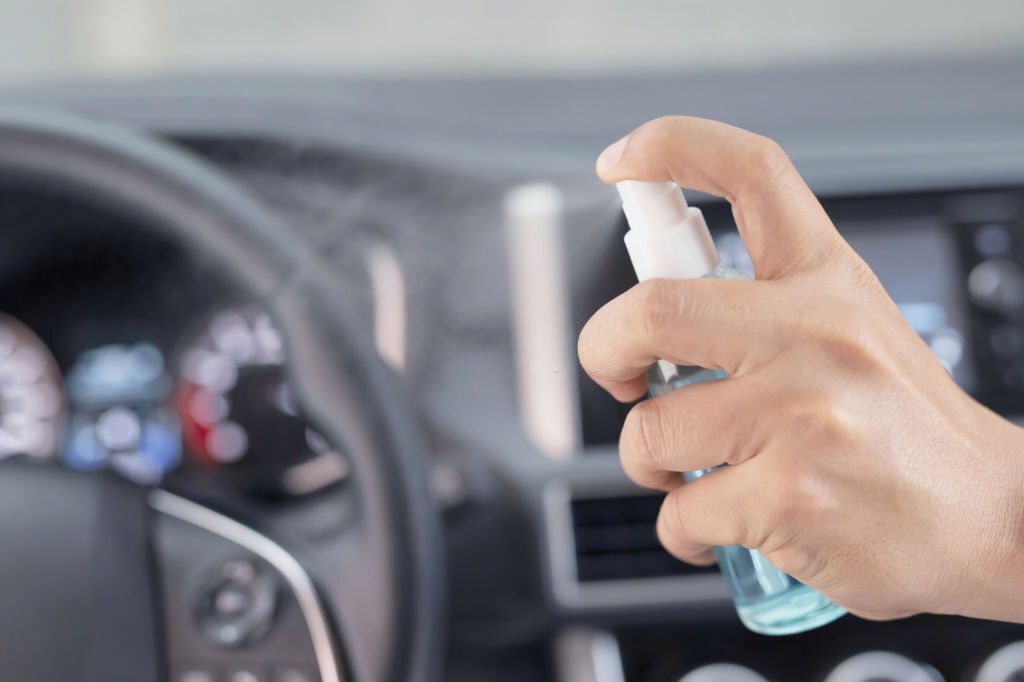 Hand of man is spraying alcohol,disinfectant spray on steering wheel in her car,prevent infection of Covid-19 virus,contamination of germs or bacteria,wipe clean surfaces that are frequently touched