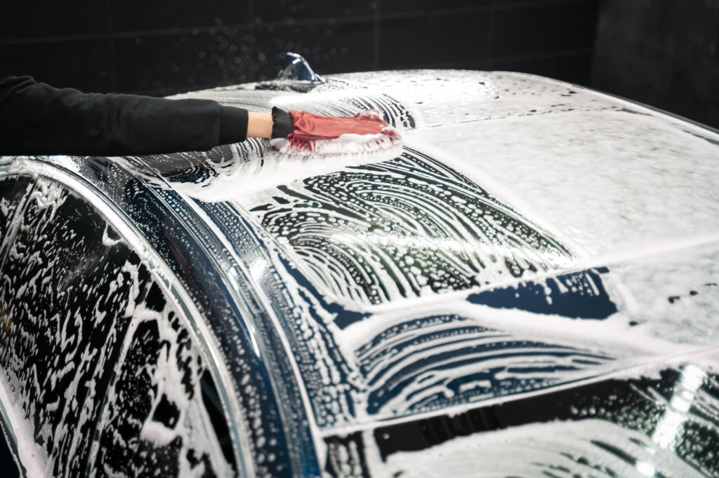 Professional car wash. Detailing worker washes the vehicle body with foam and rag