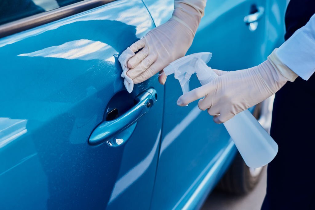 Woman disinfects car door handle with an antibacterial spray. Car washing