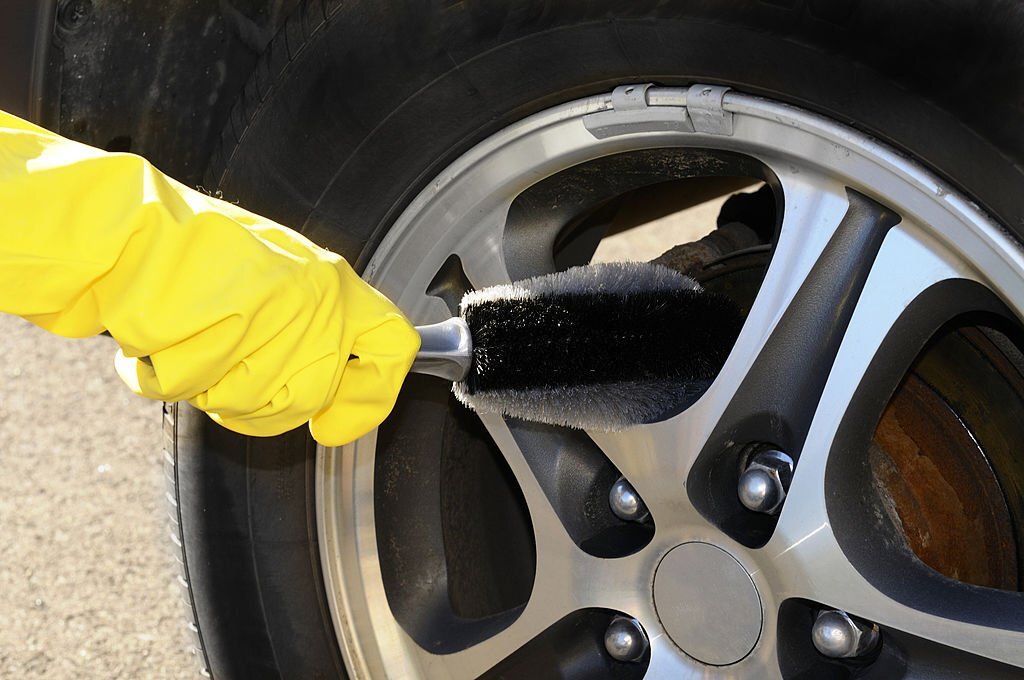 Woman's hand with a rim brush cleaning a wheel of an SUV car