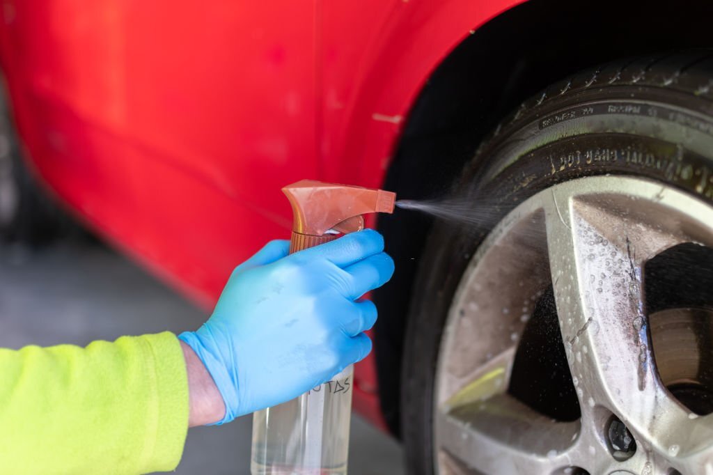 hand with blue glove doing wheel cleaning with spray liquid