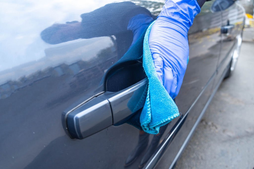 A woman's hand in a blue glove rubs the door handle. Car cleaning